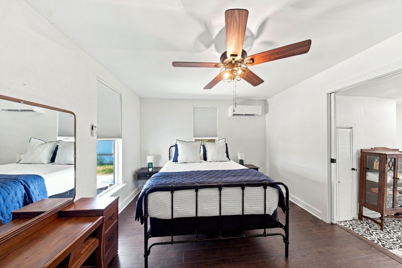 A bedroom with a bed, bedside tables, a dresser, a ceiling fan, and a door.