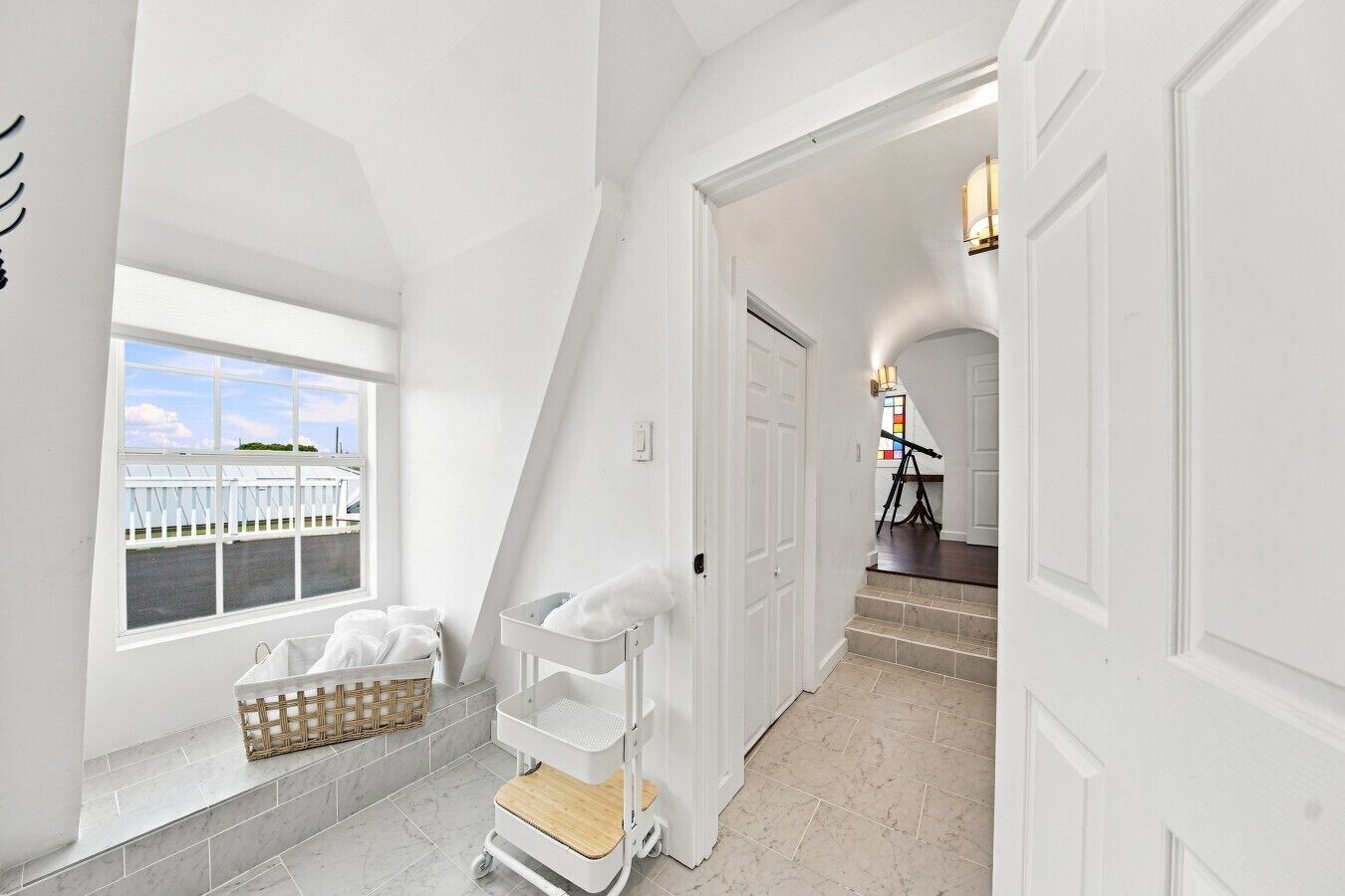 A hallway with white walls, a window with a view of a fence, and a white cart with towels.