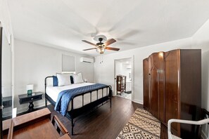 A bedroom with a bed, a wooden wardrobe, a nightstand, a desk, a chair, a ceiling fan, and a patterned rug. - The 1890 House where History meets the Horizon (Rockport)