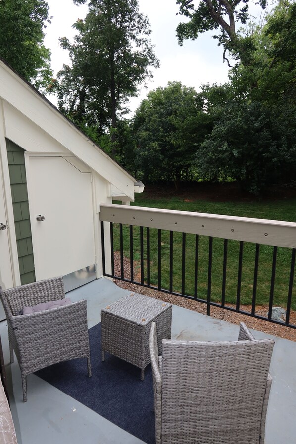 A patio area with wicker furniture, a white door, and a view of a green lawn and trees.