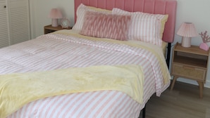 Quarto com cabeceira estofada em tom rosa, colcha listrada e duas mesas de cabeceira com abajures.