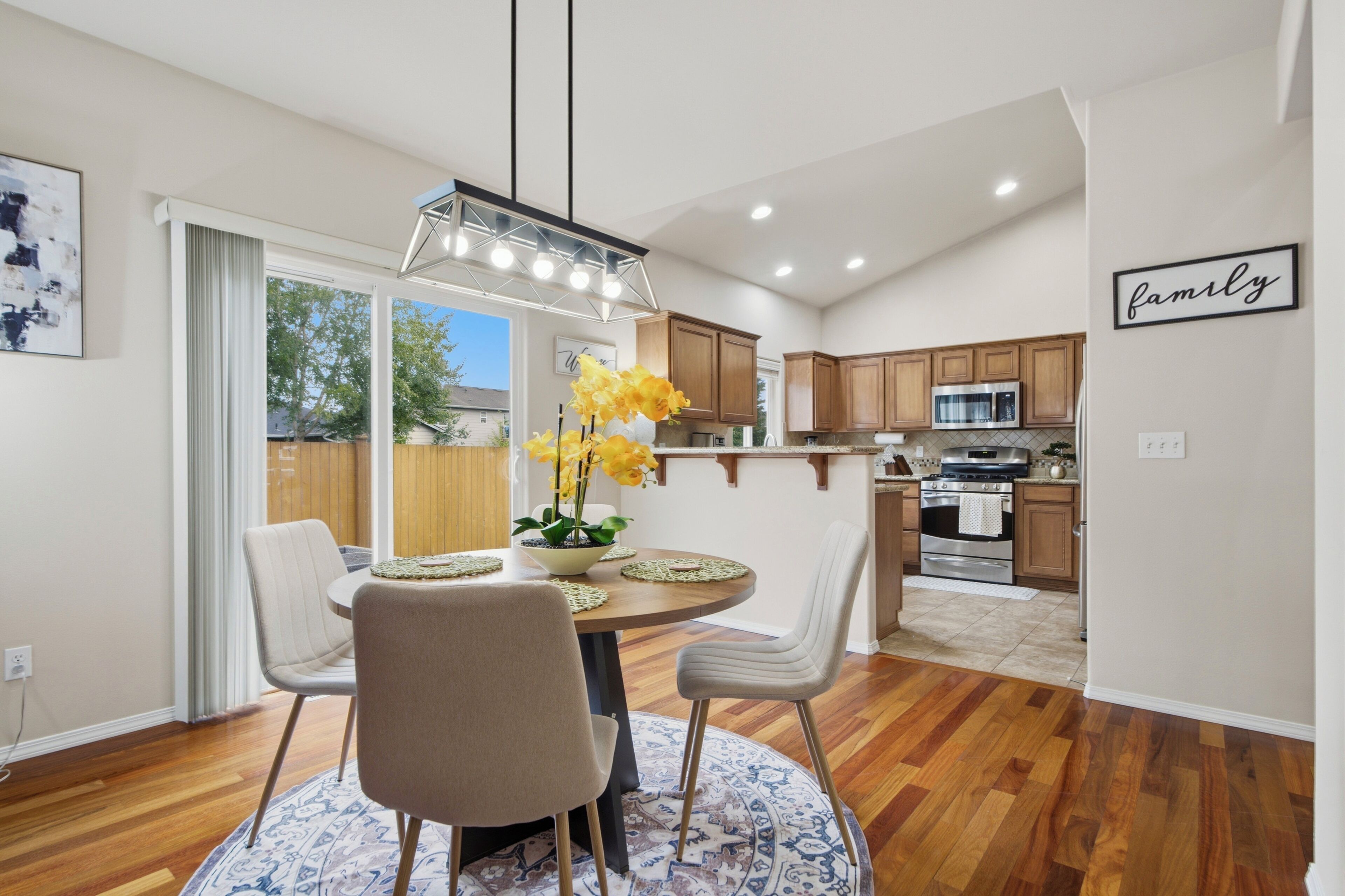 A modern kitchen with wooden cabinets, a stainless steel oven, and a dining area with a round table and chairs.