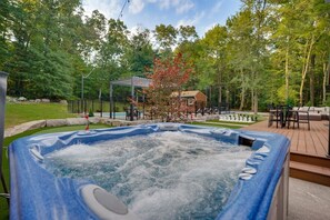 Un jacuzzi rodeado por una terraza, un pabellón y una zona de piscina con mobiliario exterior.