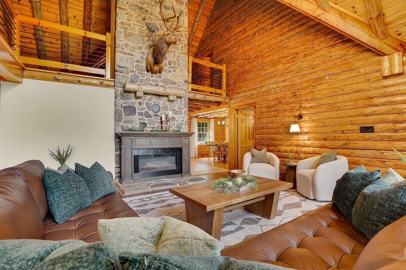 A log cabin interior with a stone fireplace, leather sofas, and a wooden ceiling.