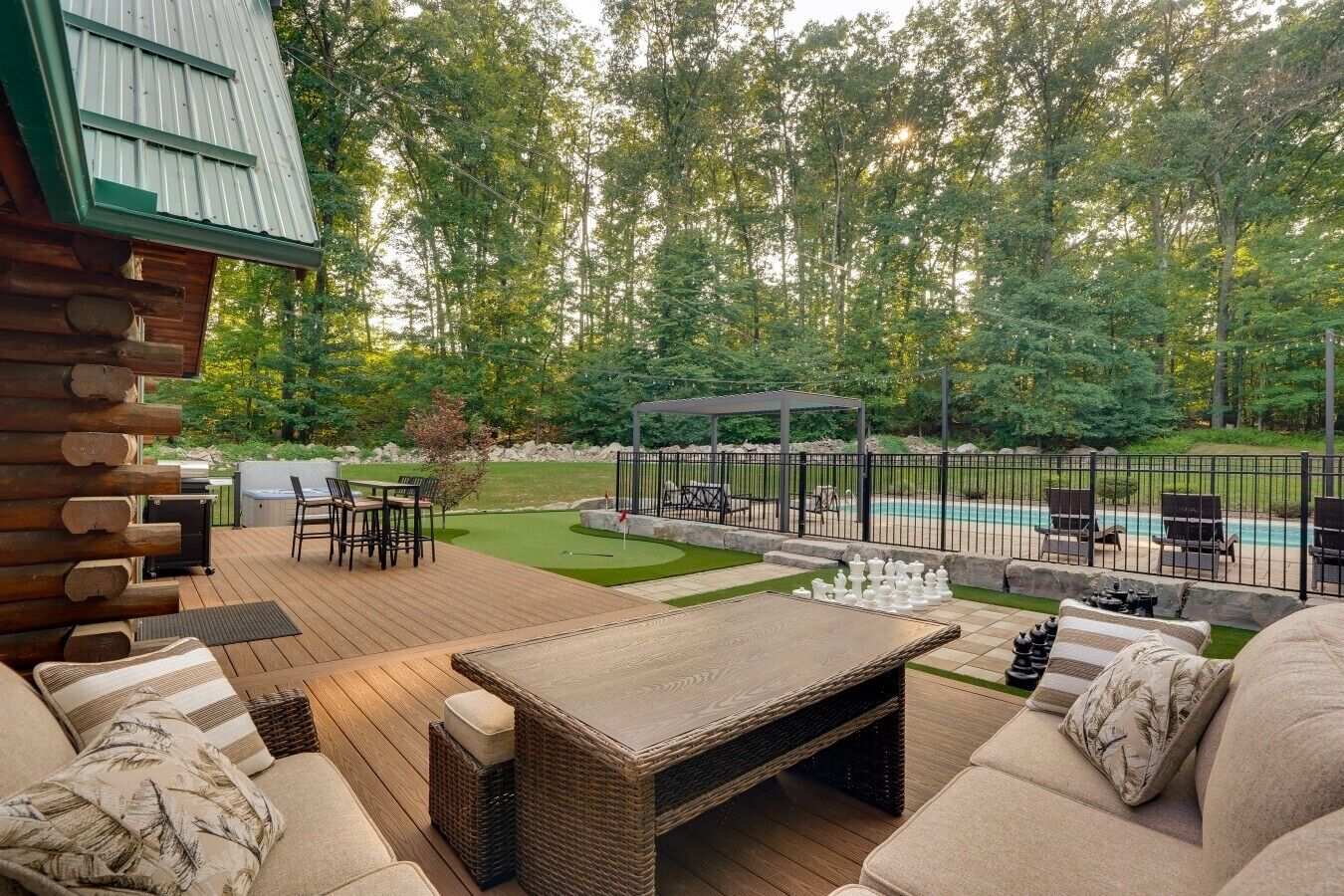 Una terraza de madera con mobiliario exterior, piscina y un pabellón.