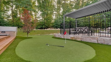 A well-maintained artificial green lawn with a putting green, a red flag, and a golf club.