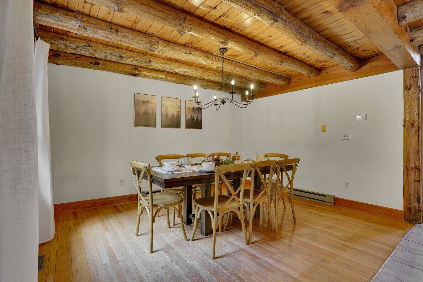 Une salle à manger avec un plafond en bois, un lustre et une table dressée pour six personnes.
