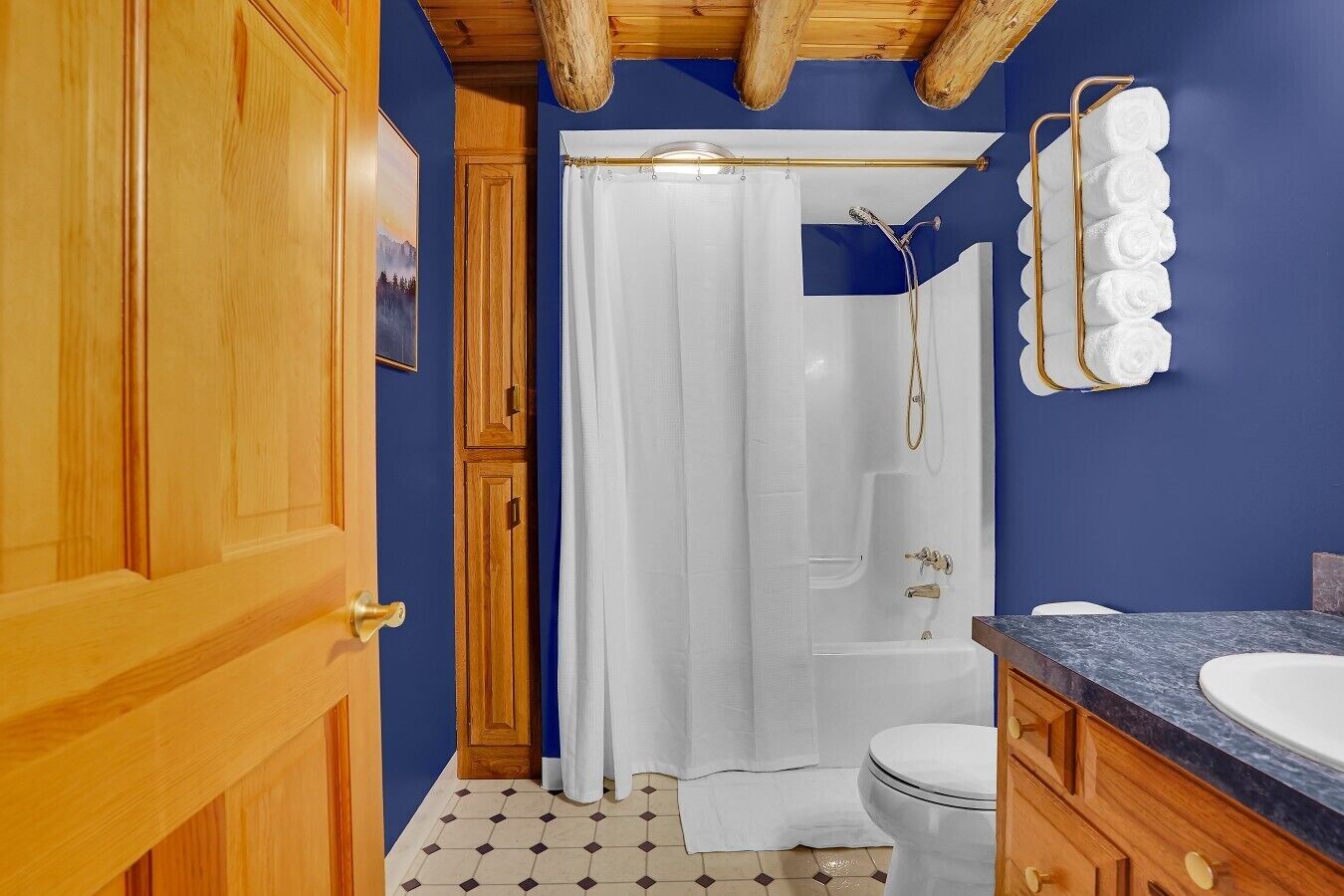 A bathroom with a wooden door, a shower curtain, a bathtub, a toilet, and a sink with a marble countertop.