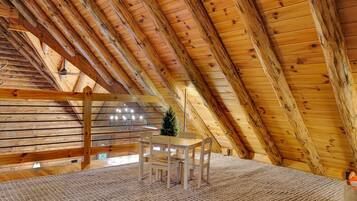 A wooden interior with a sloped ceiling, a table with chairs, and a small Christmas tree.
