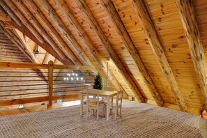 Interior de madera con techo inclinado, una mesa con sillas y un pequeño árbol de Navidad.