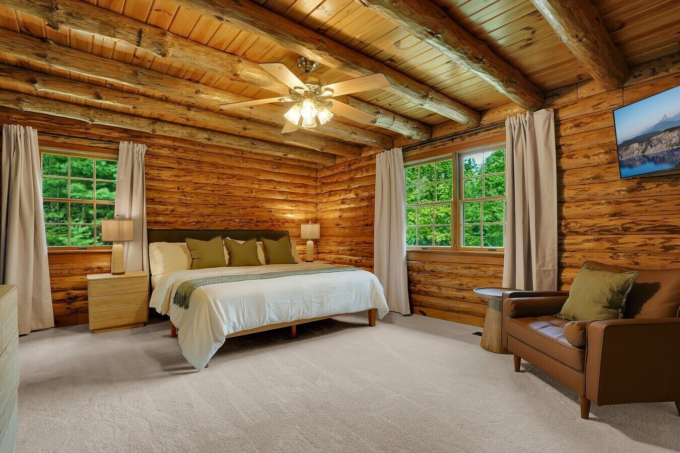Une chambre située dans une cabane en rondins, comprenant un lit, des tables de chevet, un canapé, un ventilateur de plafond et une fenêtre avec des rideaux.