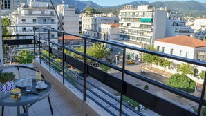 Un balcón con una mesa, sillas y vistas a un paisaje urbano con edificios y montañas.