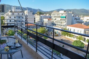 Ein Balkon mit Tisch, Stühlen und Blick auf eine Stadtlandschaft mit Gebäuden und Bergen.