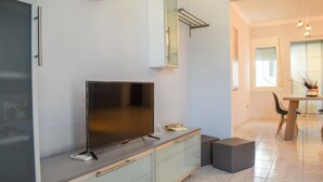 Una cocina moderna con televisor de pantalla plana, un mueble pequeño y un área de comedor con mesa y sillas.