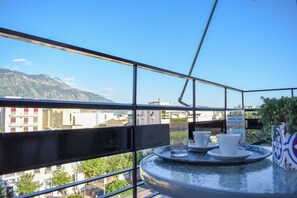Ein Balkon mit einem Tisch für zwei Personen, mit Blick auf eine Stadtlandschaft aus Gebäuden und Bergen.