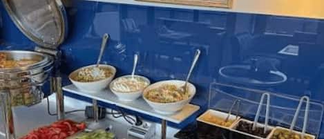 Montaje de bufé con diversos alimentos y una olla caliente sobre una estufa.
