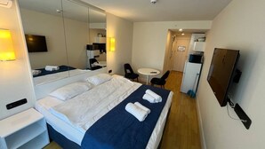 A hotel room with a large bed, a bedside table, a mirror, a TV, and a small desk with a chair. - orbi city (Batumi)