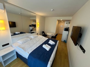 A hotel room with a large bed, a bedside table, a mirror, a TV, and a small desk with a chair. - orbi city (Batumi)