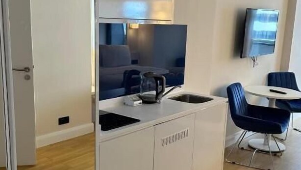 A modern hotel room with a mirrored wardrobe, a flat-screen TV, a small table with a kettle, and a seating area with chairs. - orbi city (Batumi)
