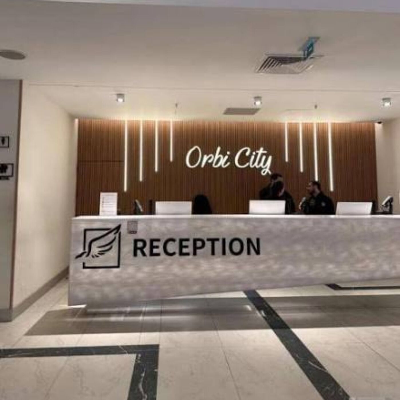 Un mostrador de recepción con un letrero que dice 'Orbi City' y un logotipo que indica zona de recepción.