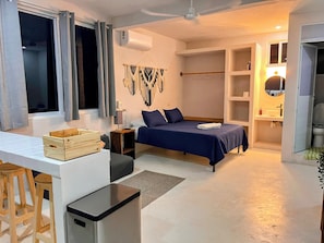 A bedroom with a bed, bedside table, lamp, and a macrame wall hanging. - Mangal Suites Vasa (Brisas de Zicatela)