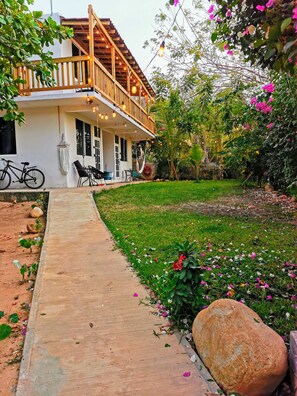 A house with a wooden balcony, a bicycle, and a garden with flowers and plants. - Mangal Suites Vasa (Brisas de Zicatela)