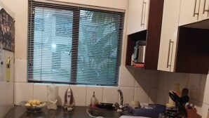 Una cocina con estufa, lavamanos y ventana con persianas.