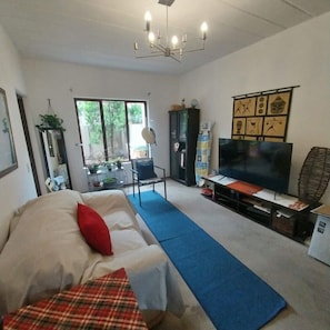 Ein Wohnzimmer mit Sofa, Fernseher, Essbereich mit Tisch und Stühlen sowie einem großen Fenster.