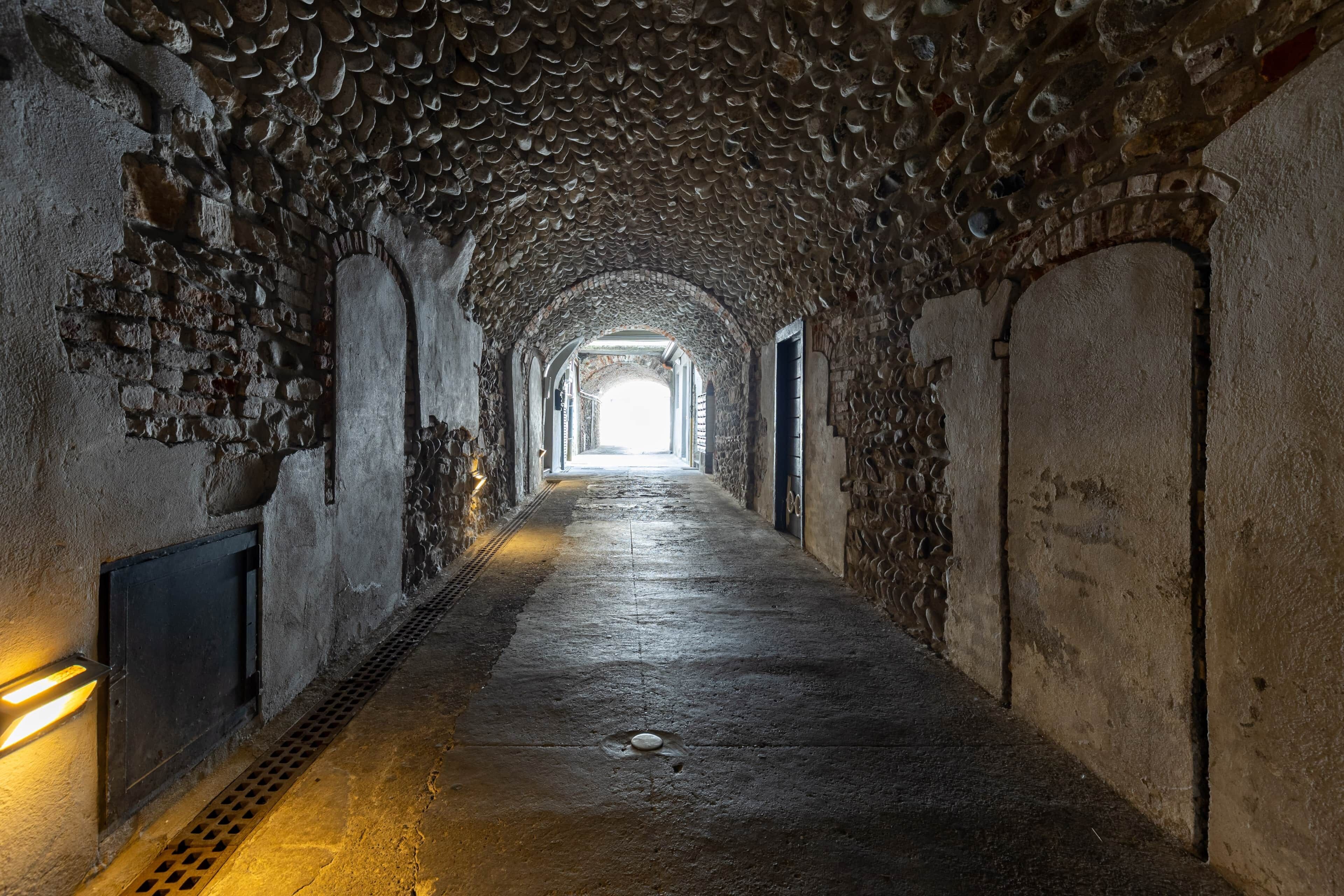 Ein steinerner Tunnel mit rauer Struktur, der zu einem helleren Bereich am Ende führt.