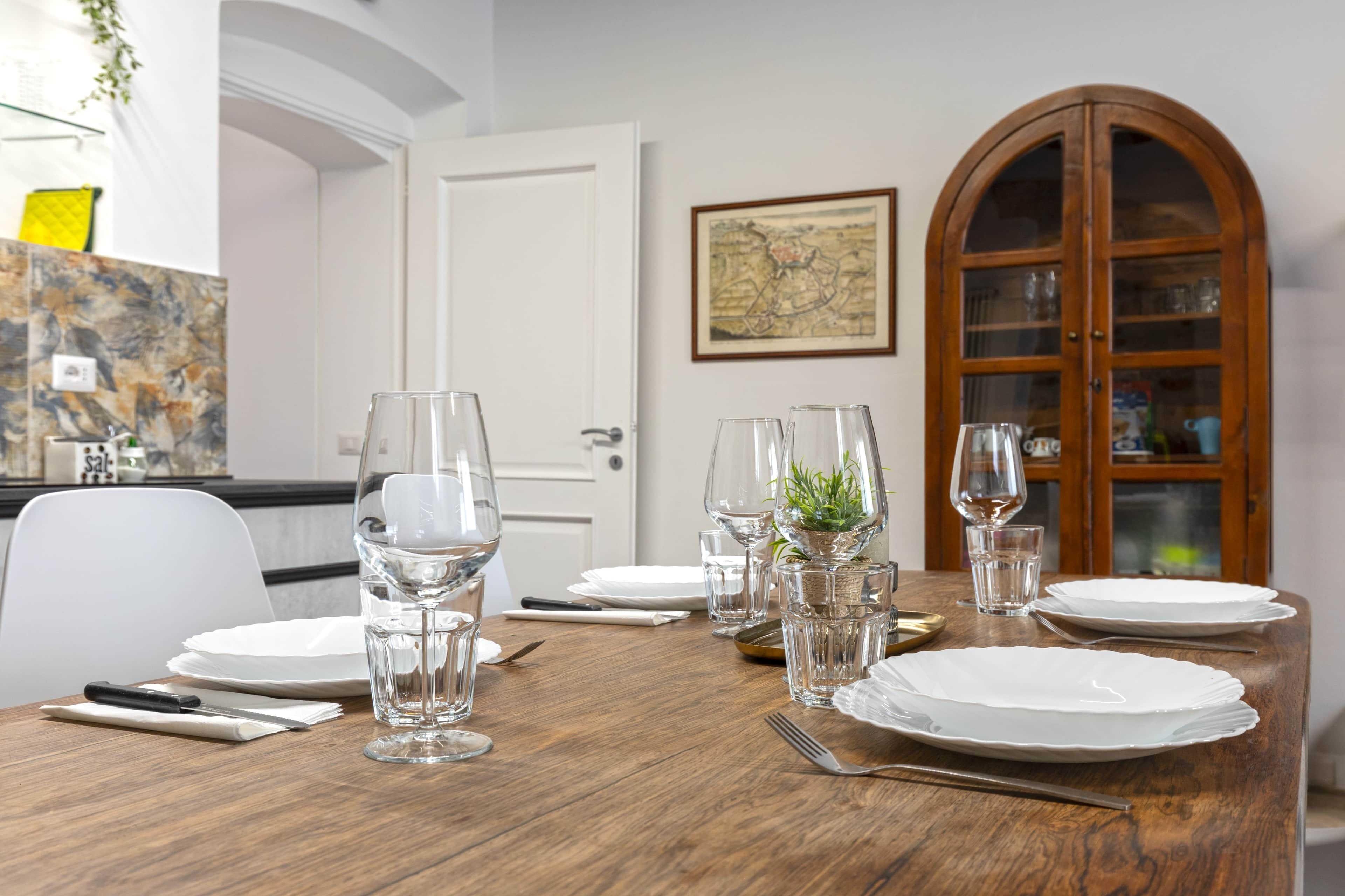 A dining table set with plates, glasses, and cutlery, a wooden cabinet with glass doors, and a map on the wall.