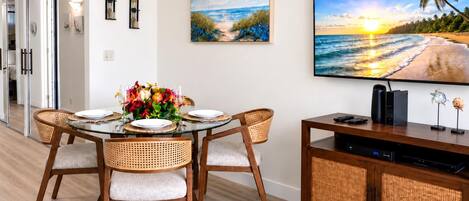 A dining area with a round table, four chairs, a vase of flowers, and a television on a wooden cabinet.