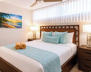 Ein Hotelzimmer mit einem Bett, zwei Nachttischlampen, einem Bild an der Wand und einem Deckenventilator.