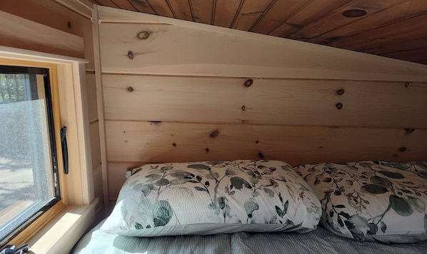 A wooden cabin interior with a bed, a window, and a view of the outdoors.