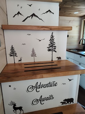 A kitchen with wooden cabinets, a countertop, and a wall decal featuring a nature scene with mountains, trees, and wildlife silhouettes.