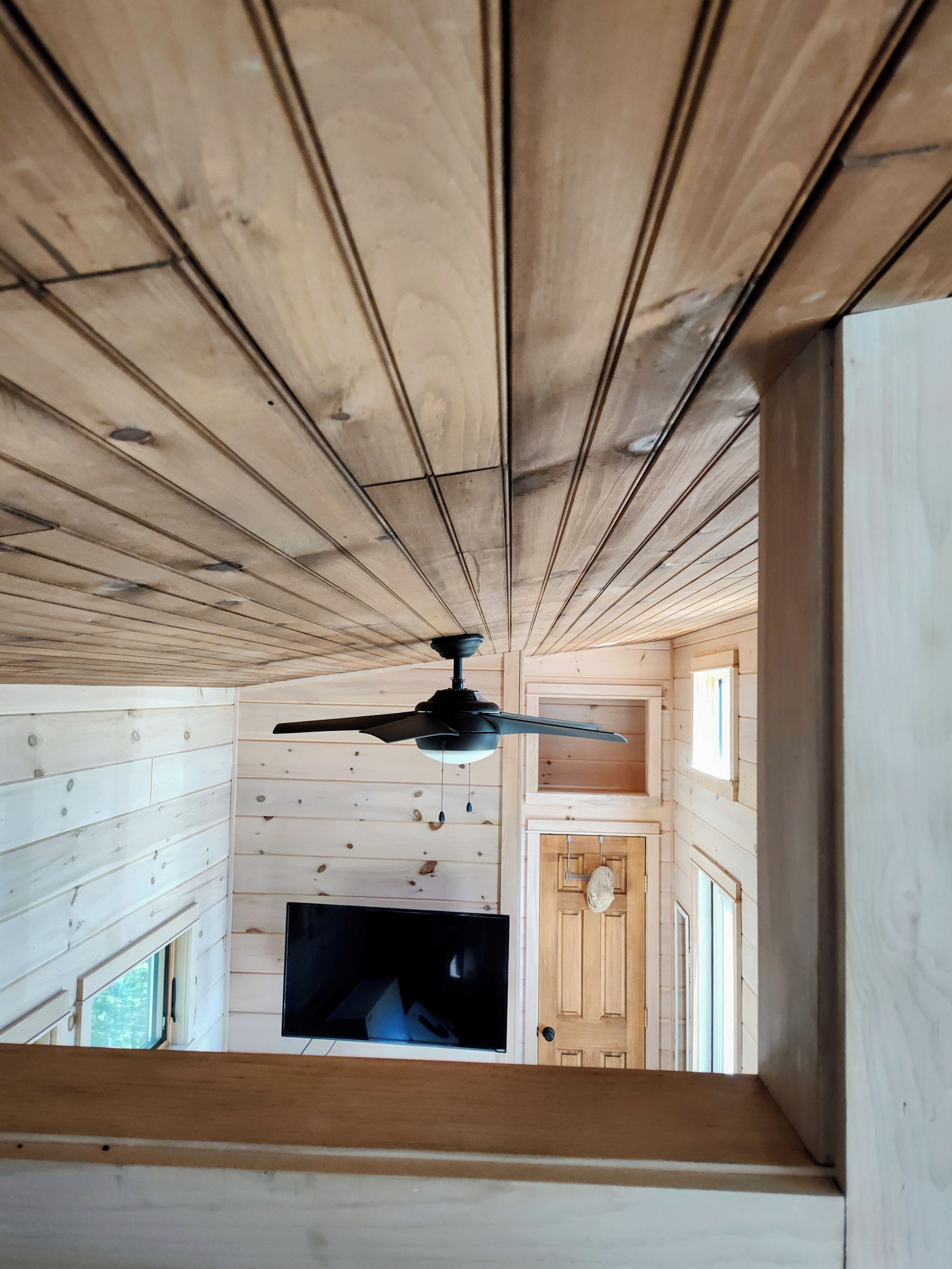 Une pièce avec un plafond en pente, un ventilateur de plafond, un téléviseur à écran plat et une porte en bois.