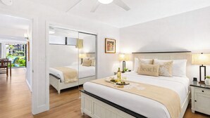 A hotel room with a large bed, a bedside table with a lamp, a mirror, and a view of the outside. - Papakea | 2 Ocean View Villas, Sleeps 8 | Car Incl. w/ 6+ Nights | ML-4265 by KBM (Lahaina)