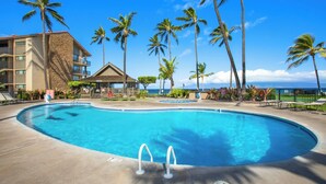 A resort pool with palm trees, a building with a stone facade, and a view of the ocean. - Papakea | 2 Ocean View Villas, Sleeps 8 | Car Incl. w/ 6+ Nights | ML-4265 by KBM (Lahaina)
