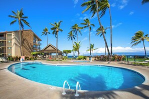 Ein Hotelpool mit Palmen, ein Gebäude mit Naturstein-Fassade und Blick auf den Ozean.