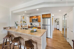 A modern kitchen with granite countertops, stainless steel appliances, wooden cabinets, and a central island with bar stools. - Papakea | 2 Ocean View Villas, Sleeps 8 | Car Incl. w/ 6+ Nights | ML-4265 by KBM (Lahaina)