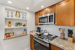 A kitchen with wooden cabinets, a stainless steel microwave, a gas stove, and various kitchen utensils. - Papakea | 2 Ocean View Villas, Sleeps 8 | Car Incl. w/ 6+ Nights | ML-4265 by KBM (Lahaina)