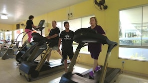 A group of people using treadmills in a gym with yellow walls and large windows. - Rosa Spa e Pousada (Aparecida de Goiânia)