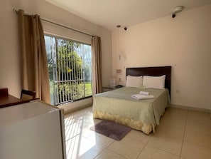 A bedroom with a bed, a window with curtains, a small table, and a chair. - Rosa Spa e Pousada (Aparecida de Goiânia)