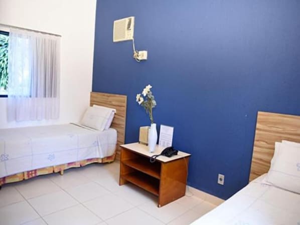 Habitación de hotel con dos camas, una mesita de noche con teléfono y un aire acondicionado instalado en la pared.