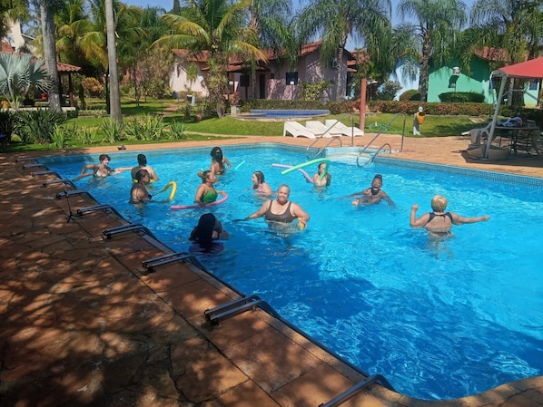 Una piscina con gente, rodeada de palmeras y un edificio con techo rojo.