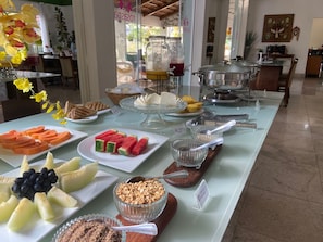 Una mesa de buffet con diversos alimentos, incluyendo frutas, pastelería y una estación de café.