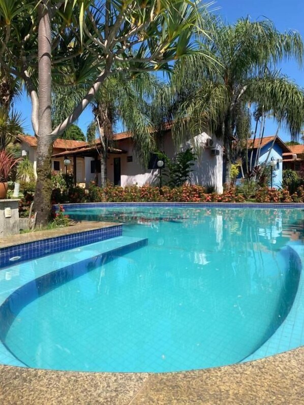 Una piscina con borde de azulejos, rodeada de palmeras y un edificio con techo rojo.