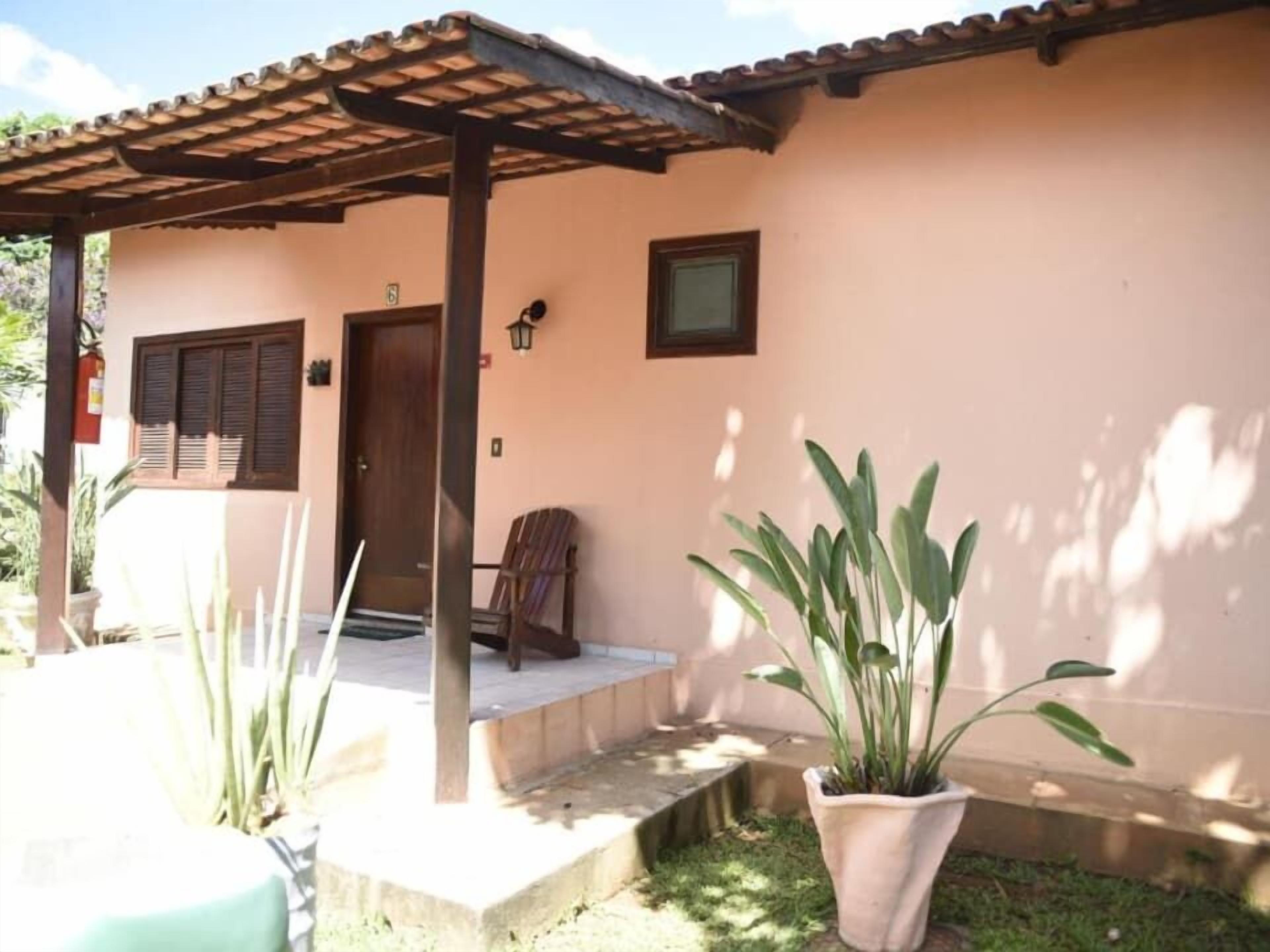 Una casa con un porche cubierto, una puerta y una ventana. Hay plantas en macetas y una silla afuera.