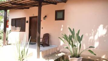 Una casa con un porche cubierto, una puerta y una ventana. Hay plantas en macetas y una silla afuera.