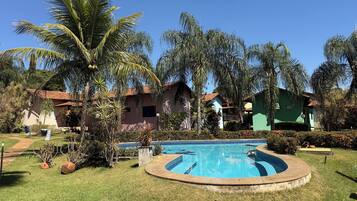 Una piscina rodeada de césped, palmeras y casas con techos de tejas rojas.
