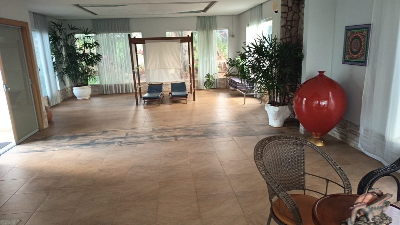 A spacious room with a wooden floor, a large red vase, and a wicker chair.